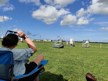My colleague Elizabeth Spicer and I watch the Blanche EM27/Sun in the new enclosure. Behind the aluminum enclosure is a line of DOE ARM equipment positioned at the La Porte airport. Identifiable pieces of equipment in that lineup from left to right include a short automated weather station and monitoring tower, a power substation, laser disdrometers, SKYRAD radiometers, a rain gauge with fence, another power substation, and shadowband radiometer.